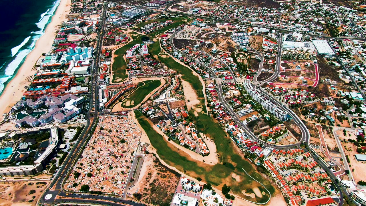 Drone view of coastal golf course beside beach and urban development.