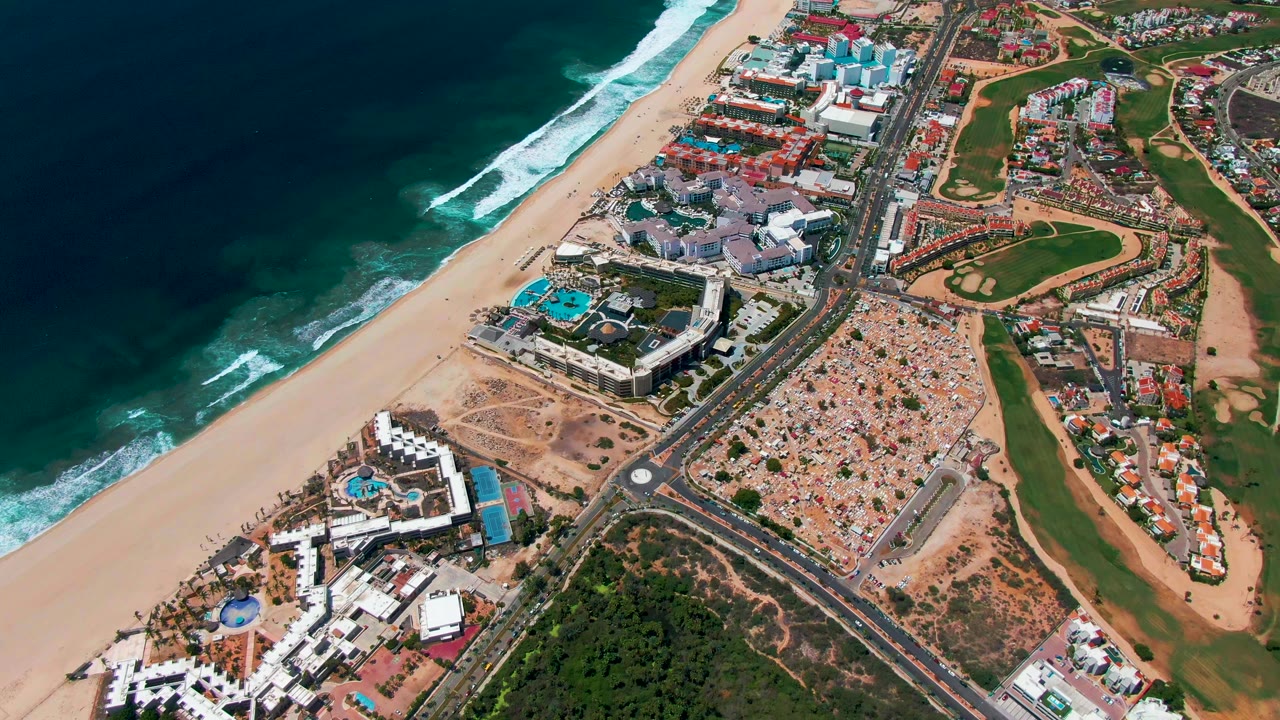Aerial coastline with beach, buildings, road junction, golf course, and cars.
