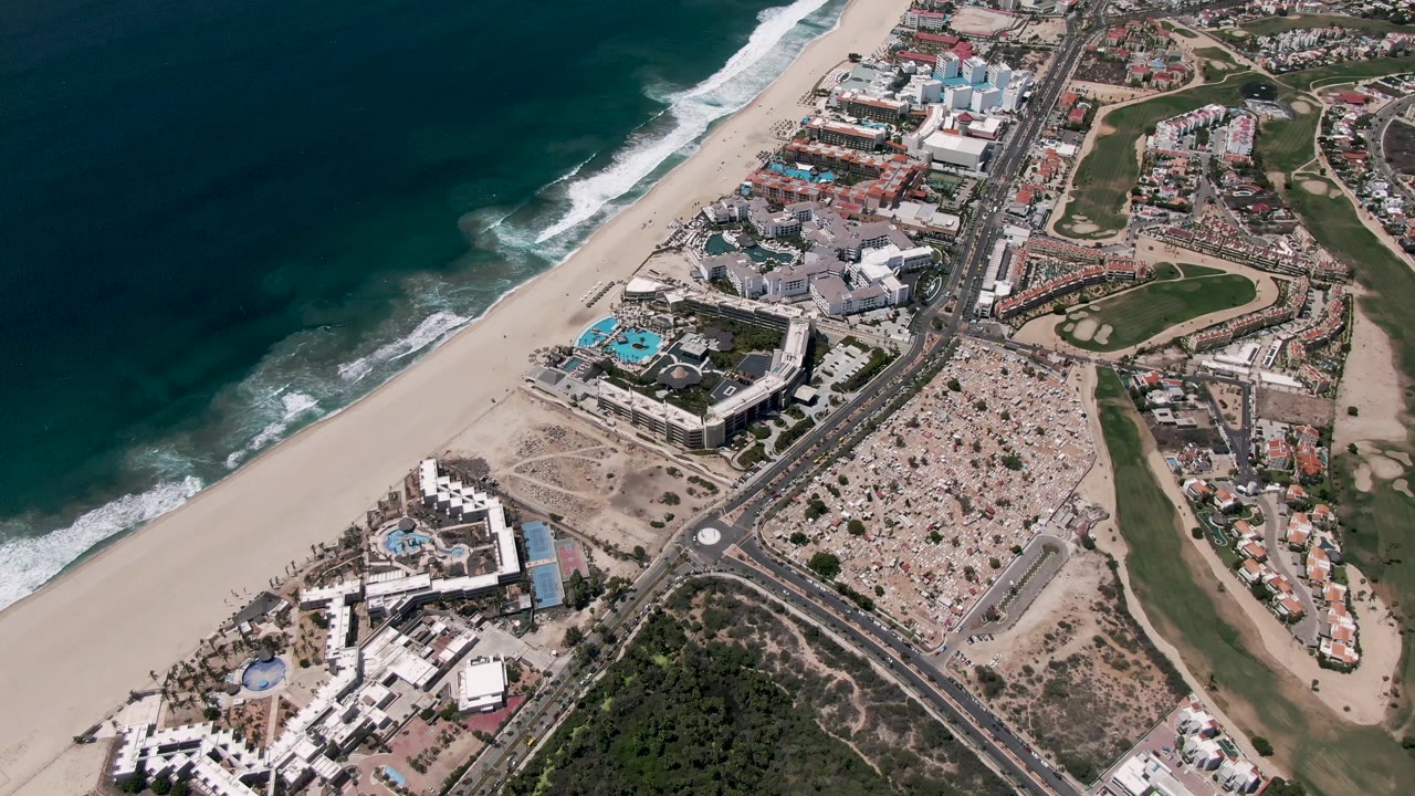 Aerial view of beach, ocean, coastal road, buildings, and golf course.