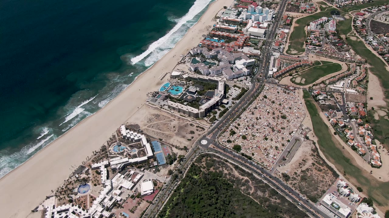 High aerial view of surf, beach, roadside buildings, and golf greens.