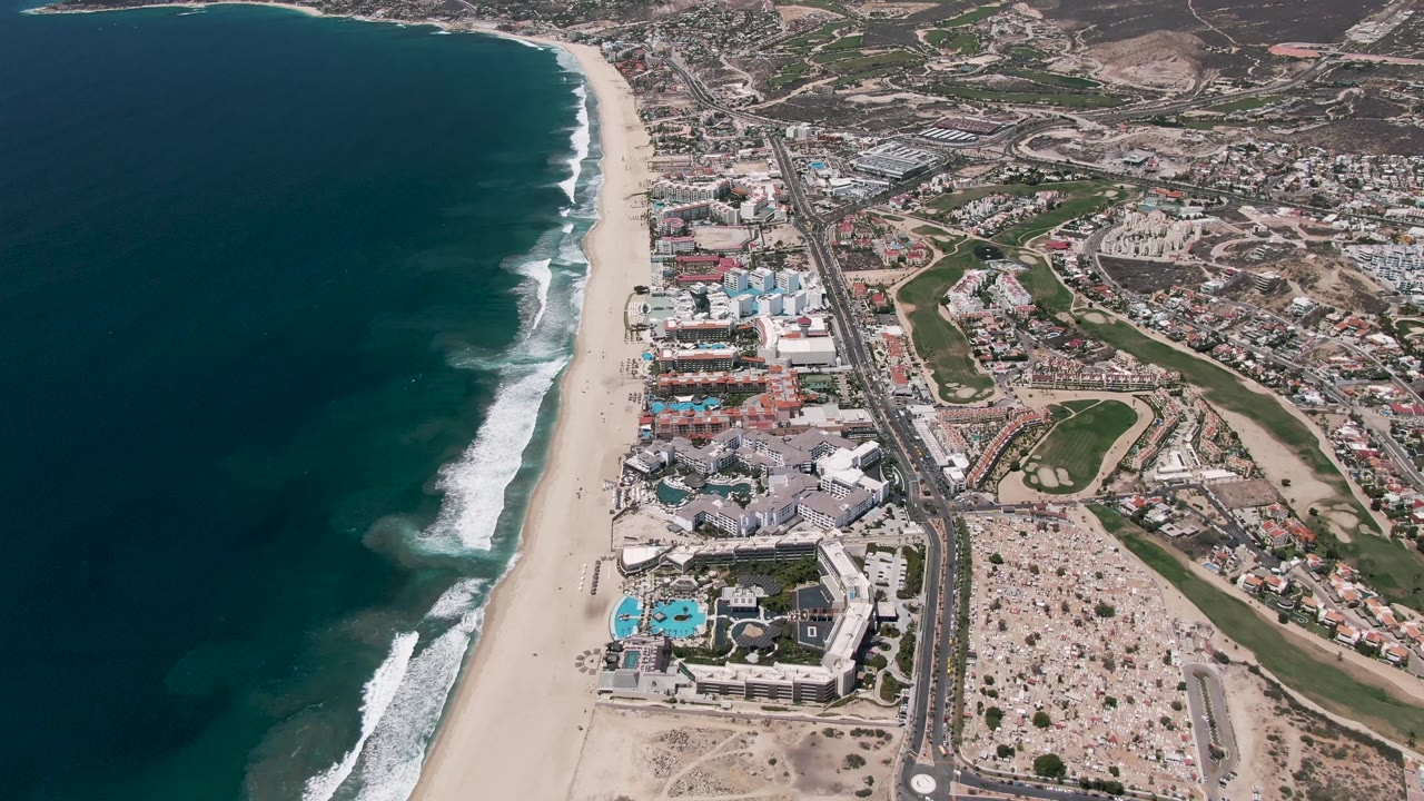 Aerial beach scene with dark ocean water, breaking waves, and developed coastline.