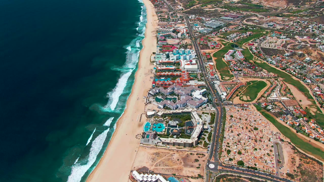 Ocean surf breaking along a long sandy beach beside a coastal road.