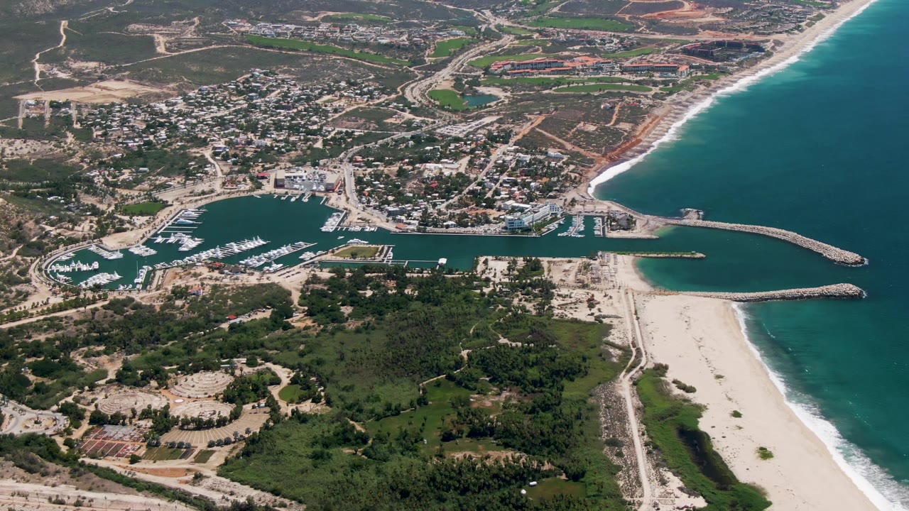 High aerial view of marina docks, beach, breakwaters, and coastal town.