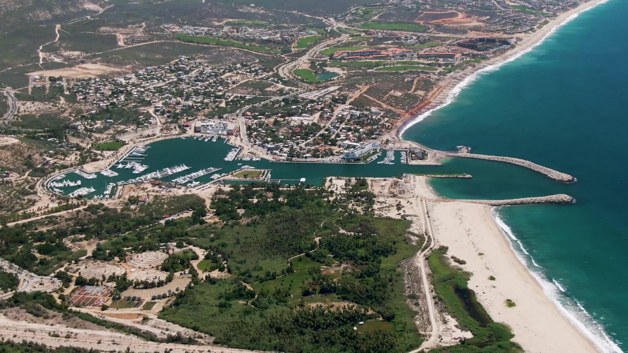 Aerial view of a coastal town, marina, sandy beach, and blue ocean.