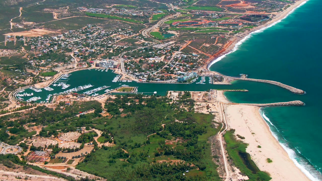 Aerial coastline with marina, surf, greenery, town, and construction sites
