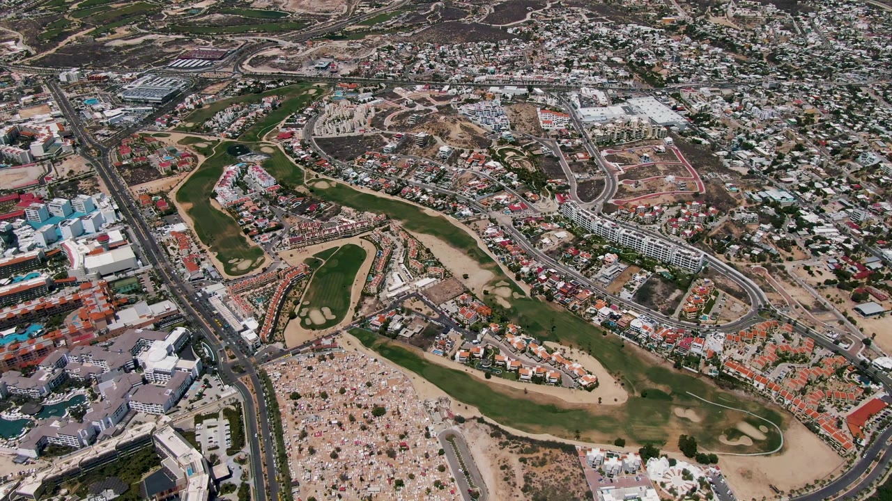 A high aerial frame over San Jose Del Cabo shows the crowded open ground, landscaped fairways, arterial roads, and tightly packed urban housing.