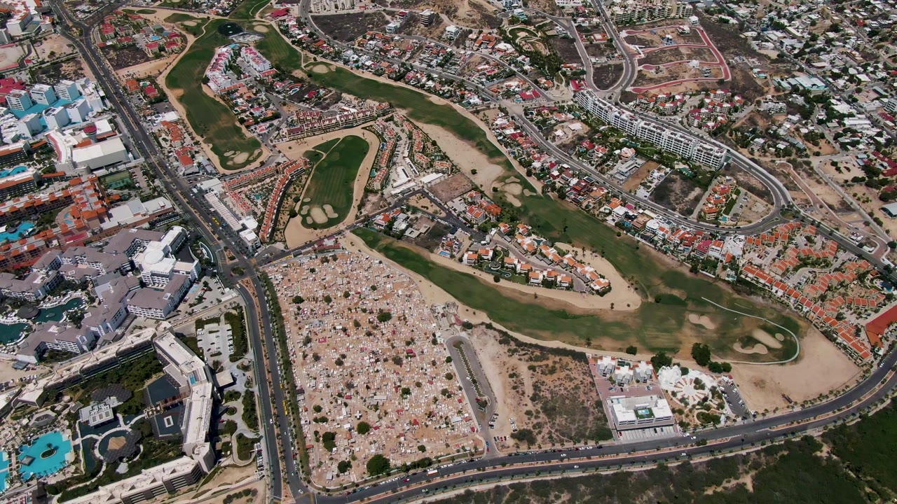 High drone frame in San Jose del Cabo showing fairways and bunkers across the center, clustered homes to the upper right, larger buildings and pools to the lower left, and no visible people.