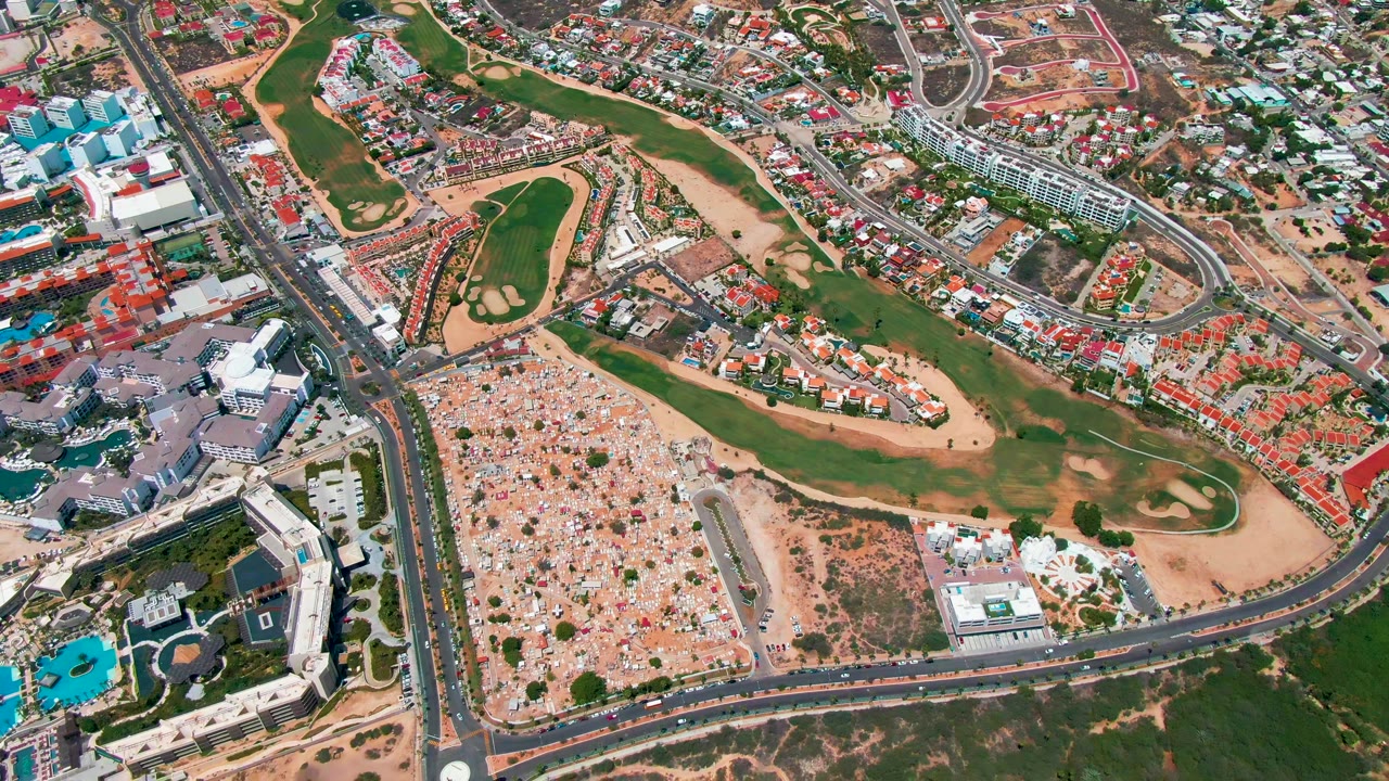 Aerial view of fairways, road intersection, residential blocks, and open sandy area.