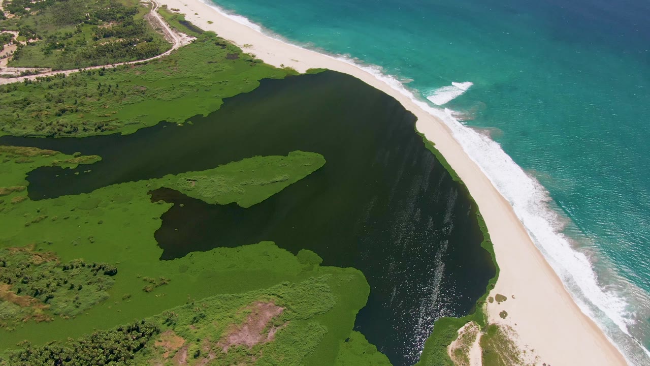 Aerial view in San Jose Del Cabo, Baja California Sur showing a green lagoon beside a white sand beach and turquoise ocean, with no visible people.