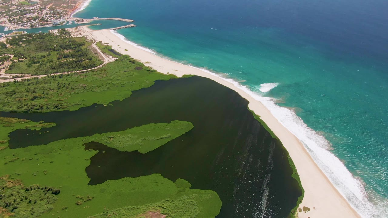 Aerial view of lagoon, sandy beach, surf, and turquoise ocean.
