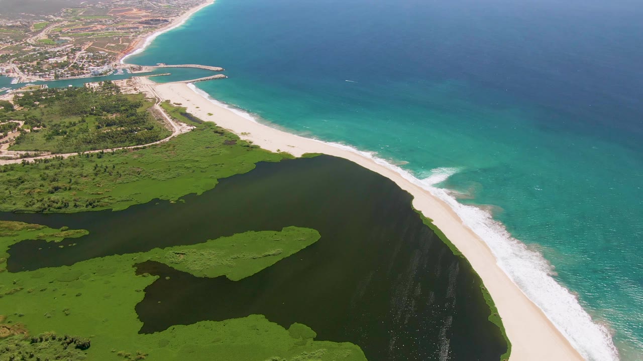 Aerial frame over San Jose del Cabo showing a pale sand beach between turquoise ocean surf and a dark green lagoon, with no visible people.