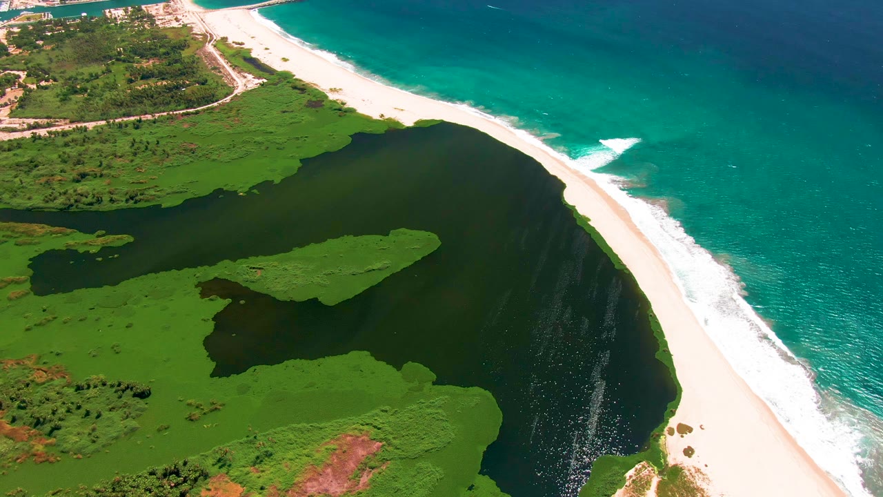 Aerial view of green lagoon, white sand inlet, and turquoise ocean surf.
