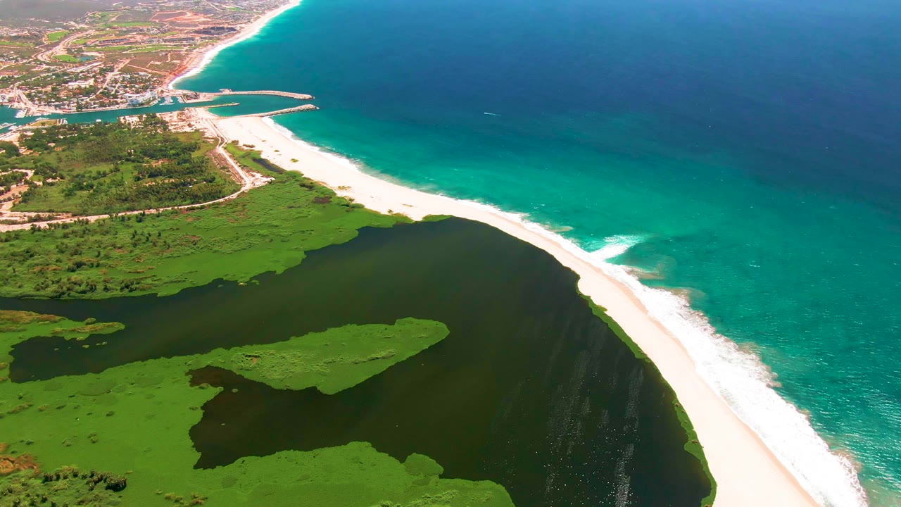 Opening aerial frame over San Jose del Cabo shows a bright sandbar between green lagoon water and turquoise ocean, with no visible people.