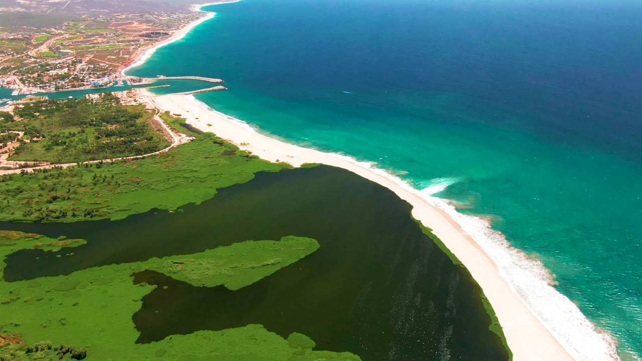 At two seconds, the aerial view shows a green island-like patch inside the lagoon below the San Jose del Cabo beach, with no visible people.