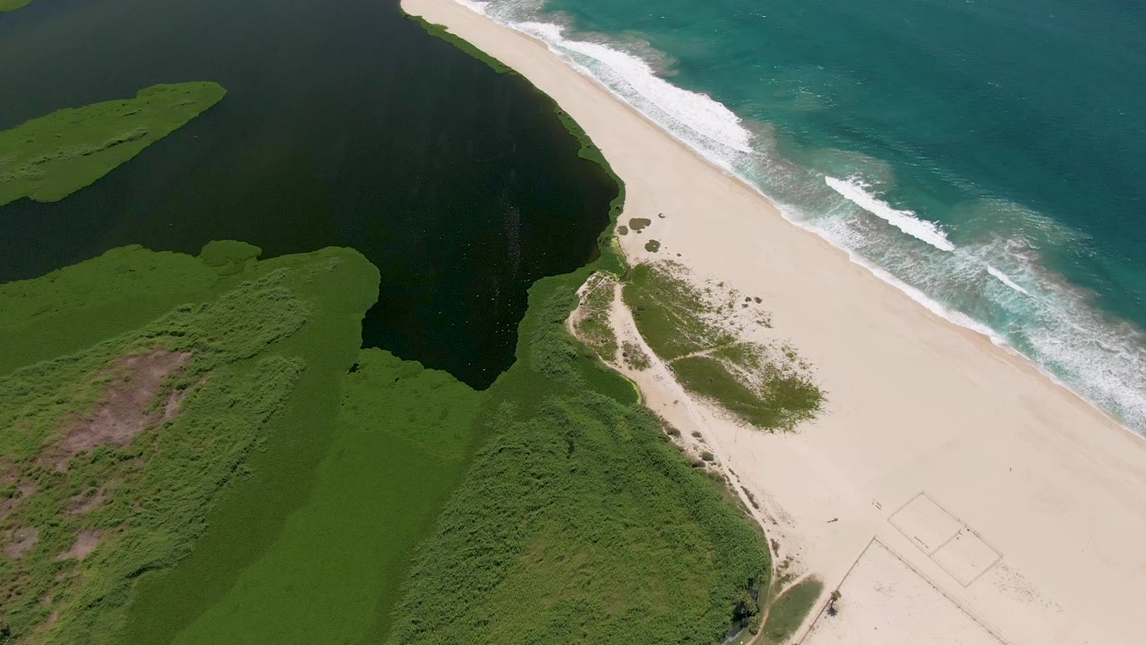Overhead coast with white waves beside a sandy beach.