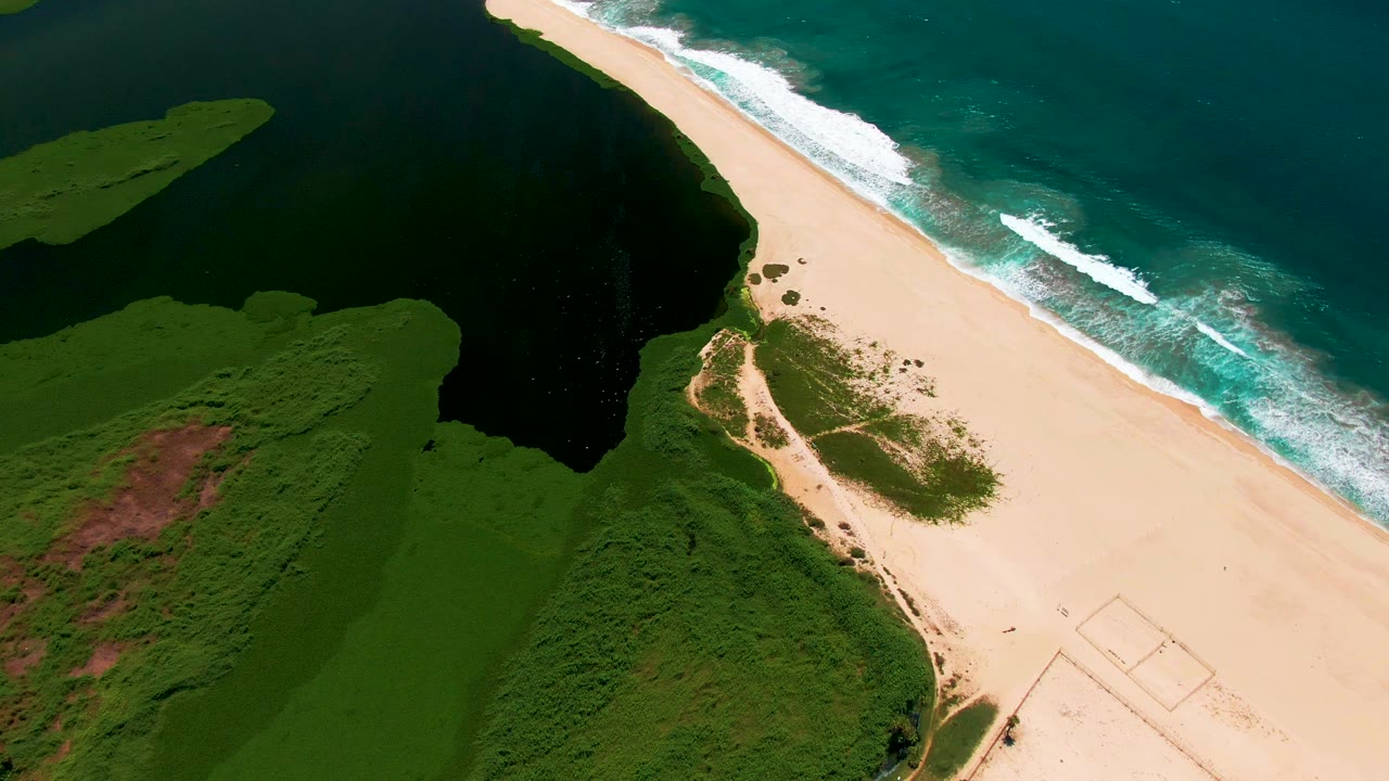 Drone view of white waves breaking beside a long sandy shoreline.