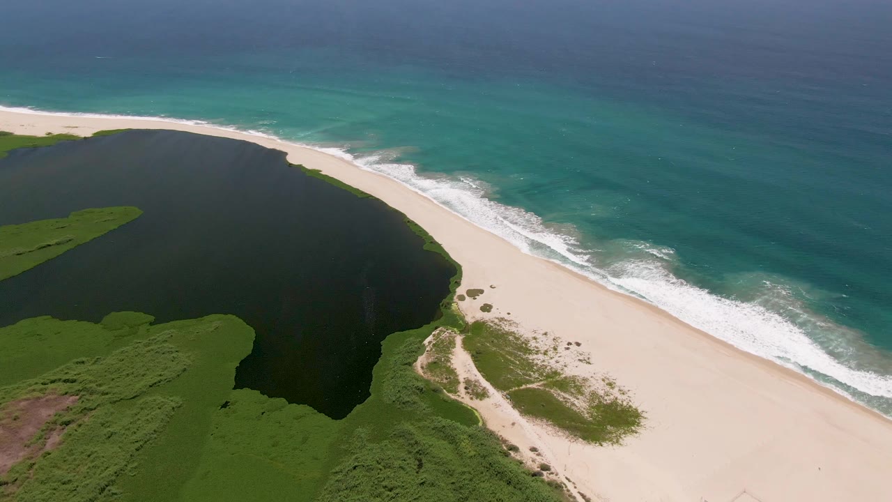 Wide aerial shoreline with lagoon, vegetation, beach, and surf