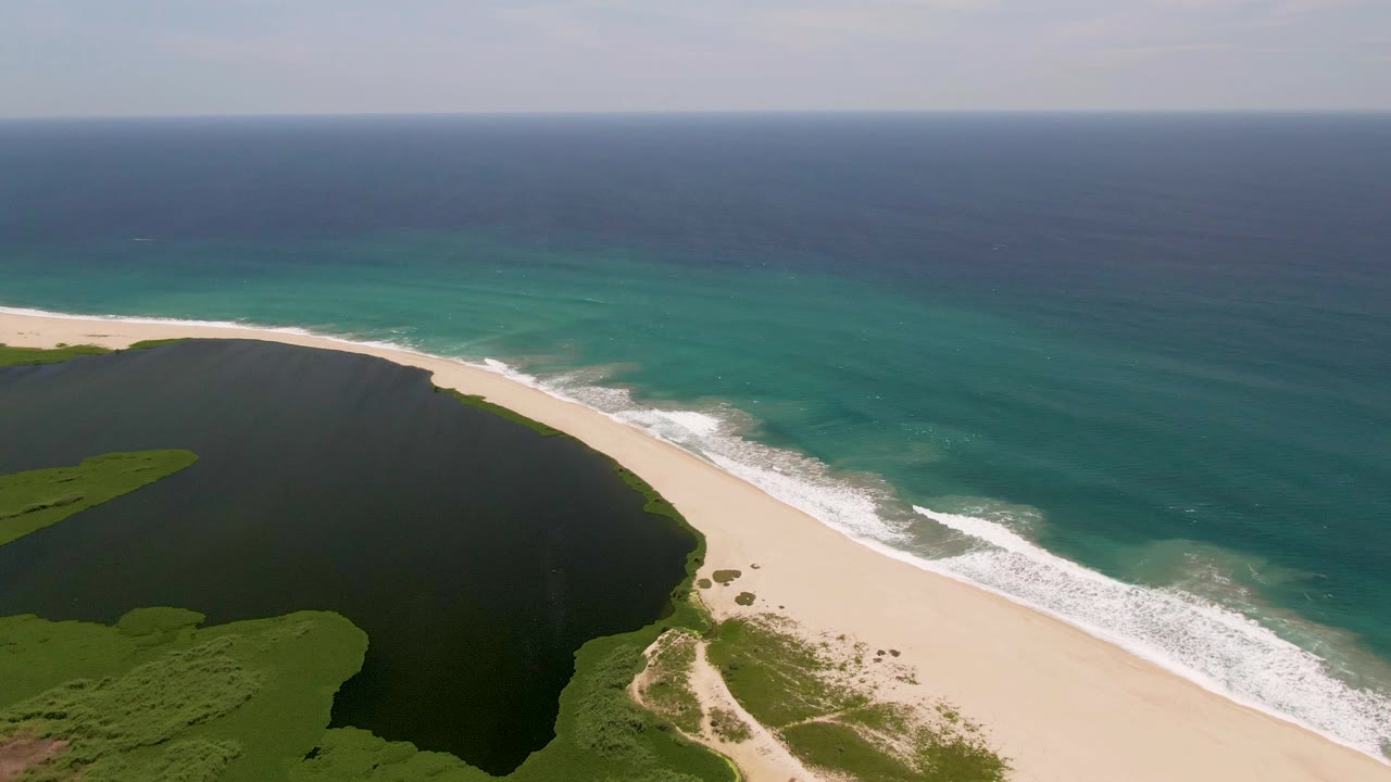 Wide aerial shoreline view with lagoon edge, beach, ocean waves, and vegetation