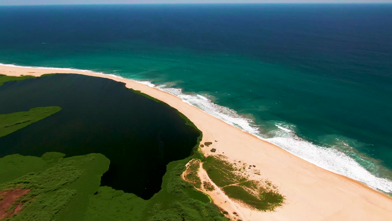 Aerial frame from San Jose Del Cabo with the curved sandy beach separating the dark lagoon from the turquoise ocean, with no visible people.