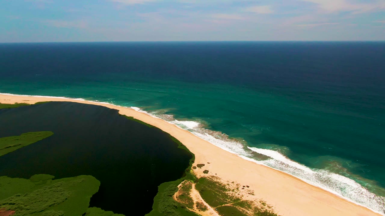 Aerial frame in San Jose del Cabo with the lagoon curving along the left side, a bright sand bar through the center, white waves on the right, and no visible people.