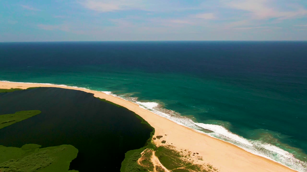 Wide aerial coastline with lagoon, sand, waves, and horizon
