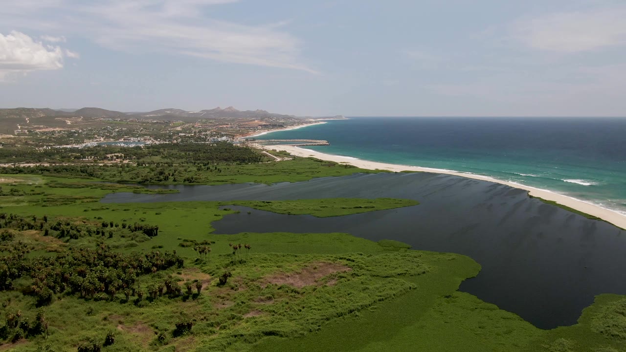 Aerial coastline showing dark lagoon water, green wetlands, pale sand, and blue ocean.