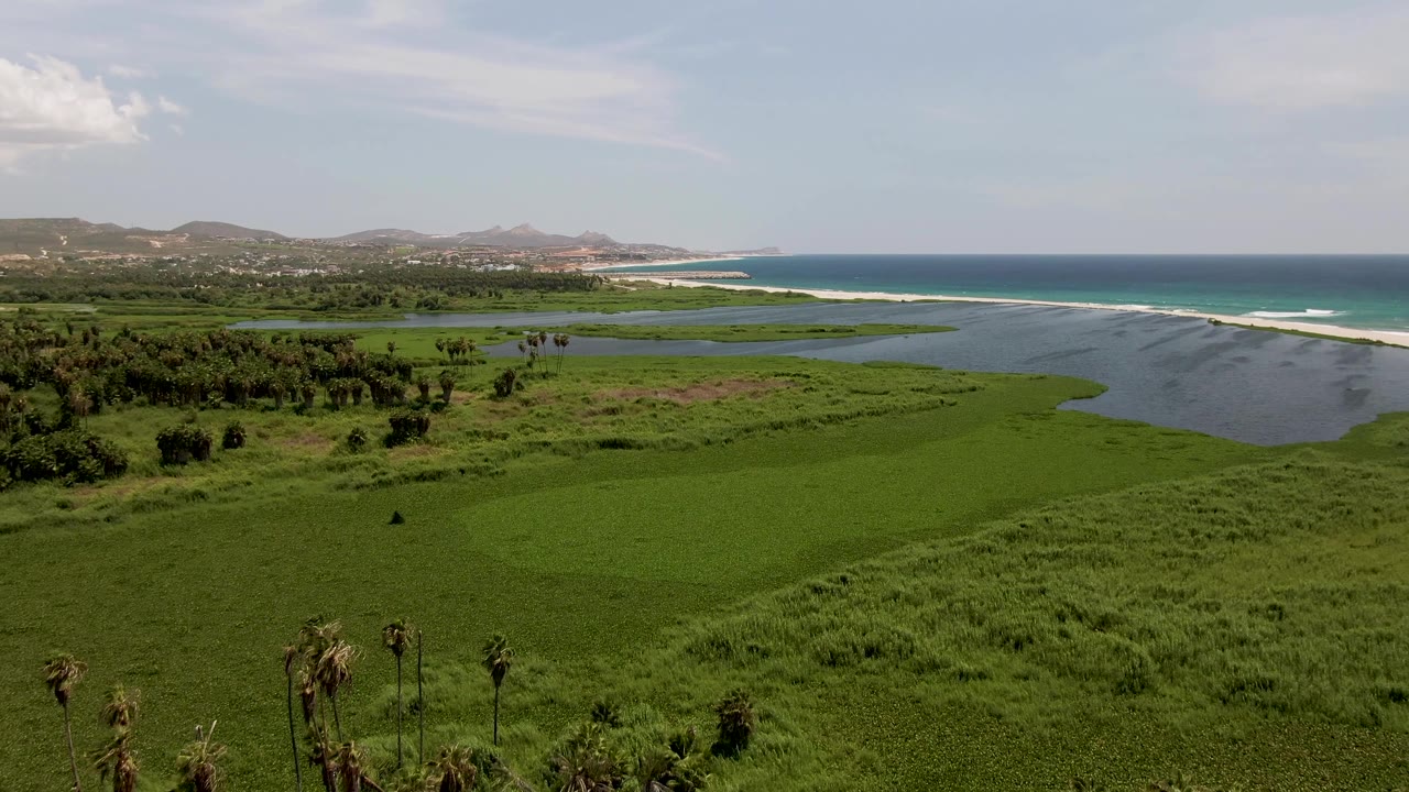 Wetlands and lagoon lead to a long beach with ocean waves beyond.