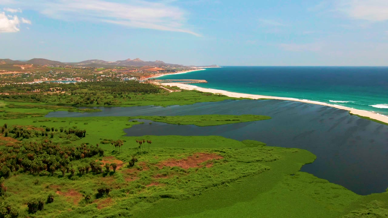 Coastal lagoon bordered by dense green vegetation and a long sandbar beach.