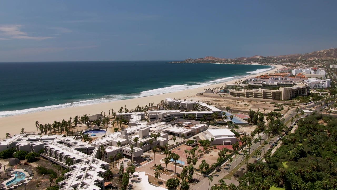 Fourth frame shows the San Jose Del Cabo shoreline from above, with more foreground greenery at the right edge, white buildings at lower left, beach and surf across the center, and no visible people.