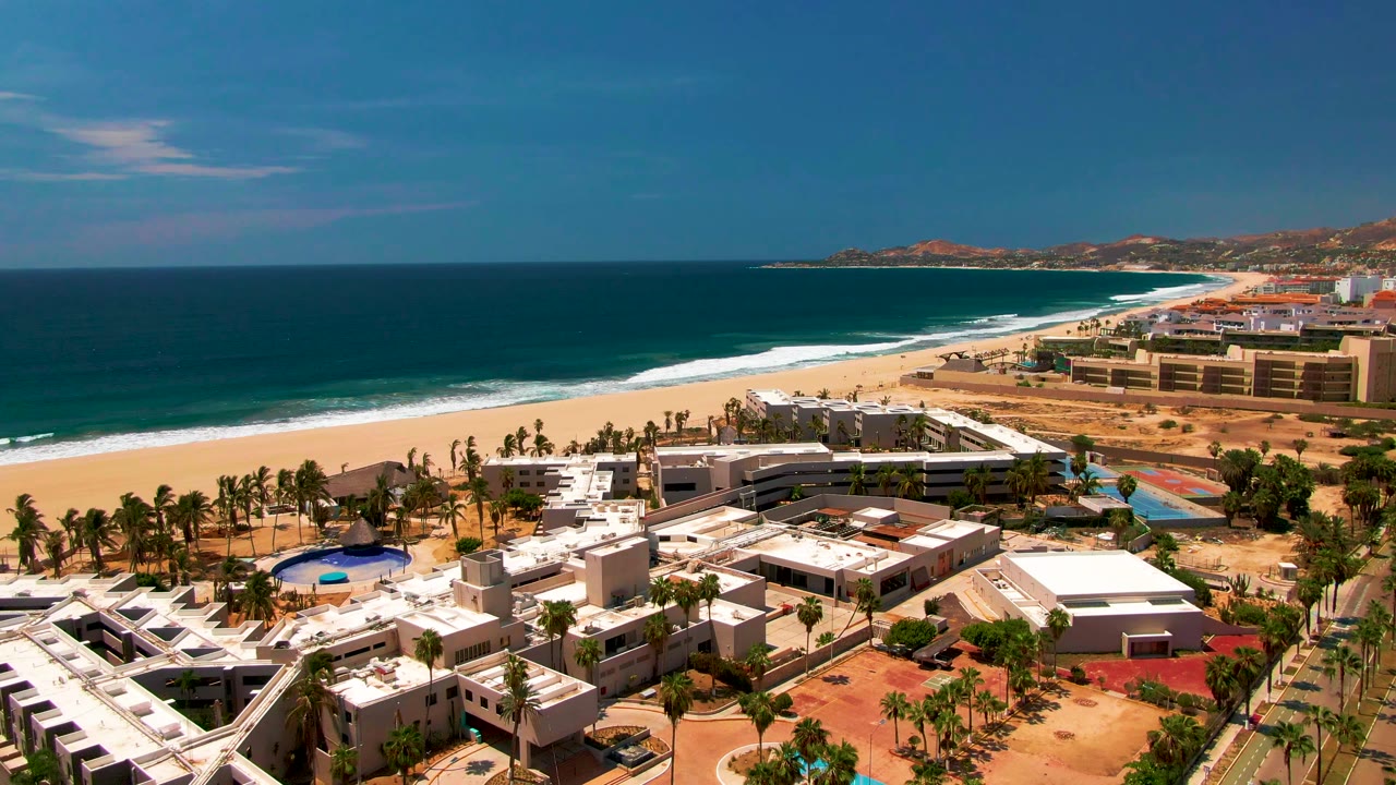 Aerial view of beach resort, coastal road, ocean, and palm trees.
