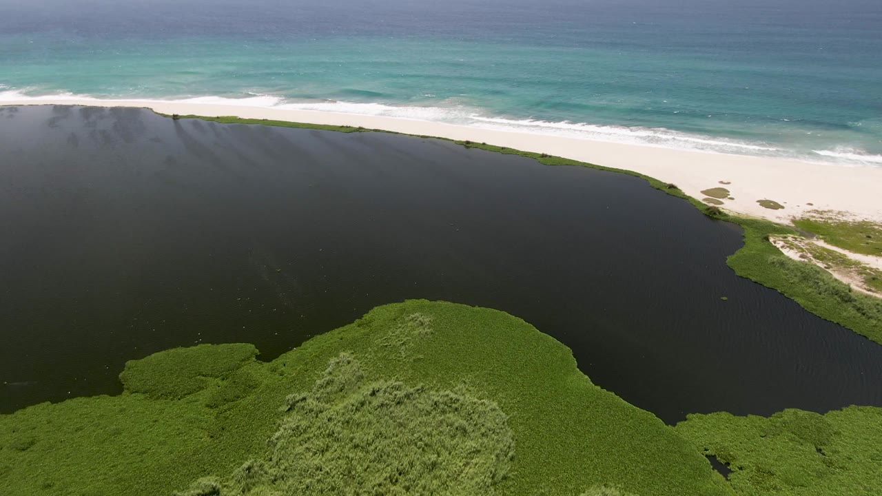 Aerial view of a dark lagoon beside white sand and turquoise ocean