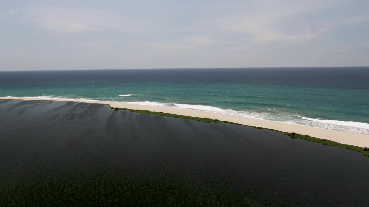 At 0:01, the San Jose del Cabo shoreline remains wide in frame as a band of white foam shifts along the pale sand, with no visible people.