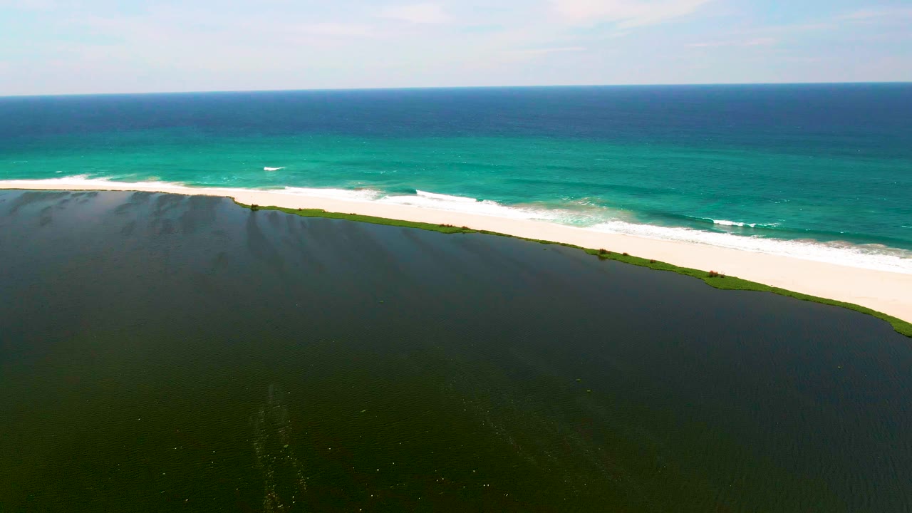 White beach arcs between still lagoon water and breaking ocean waves.