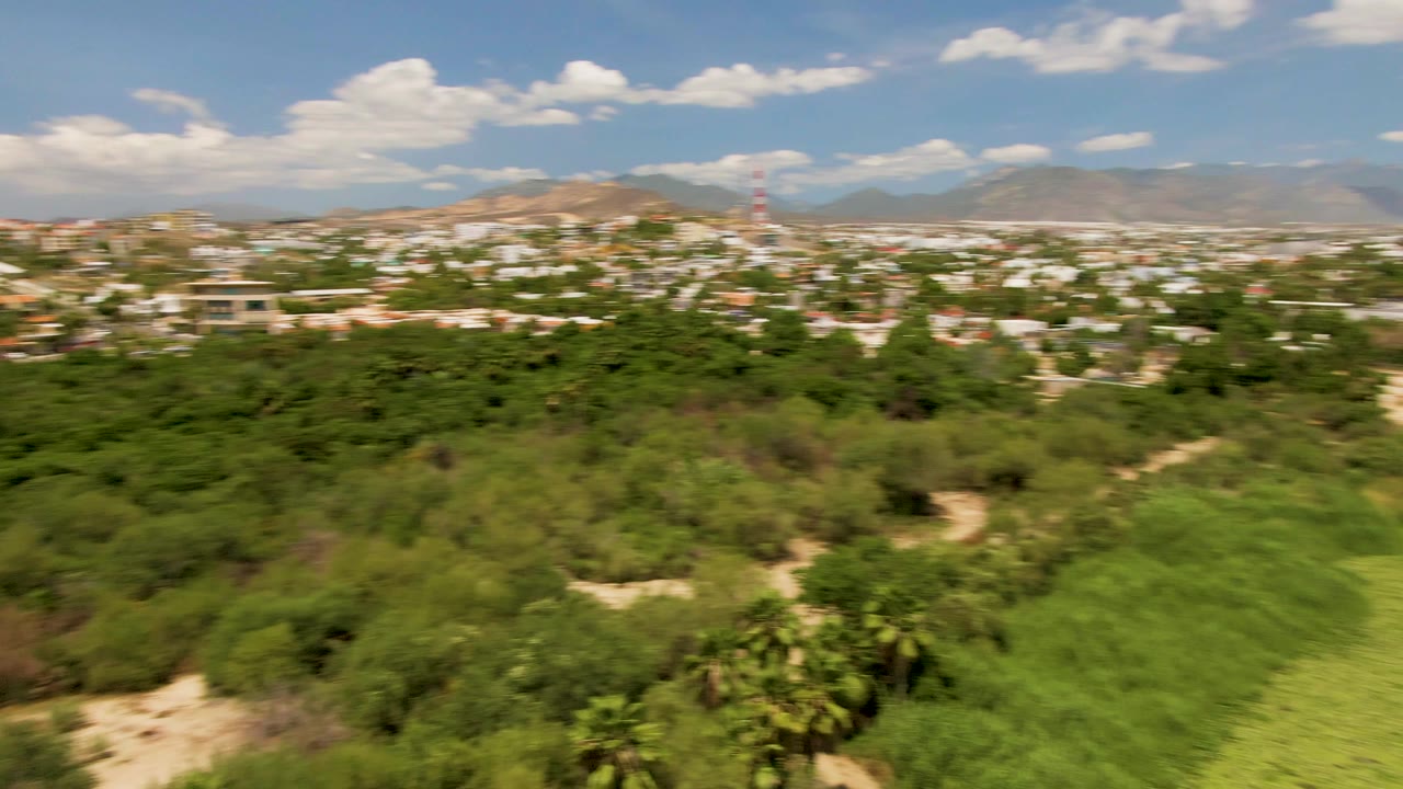 Aerial landscape with the lake receding and green vegetation leading toward a town and mountains.