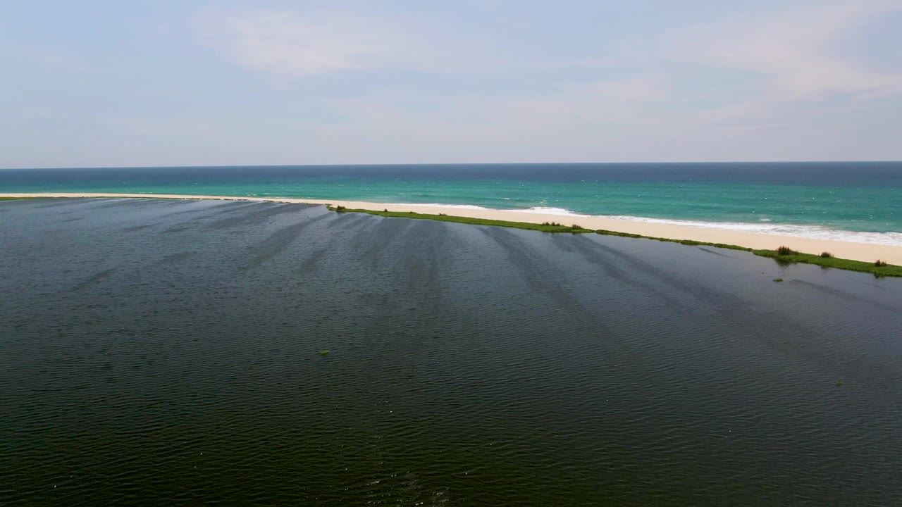 Aerial frame from San Jose del Cabo, Mexico showing dark rippled shallows in front of a pale sandbar, turquoise ocean behind it, and no visible people.