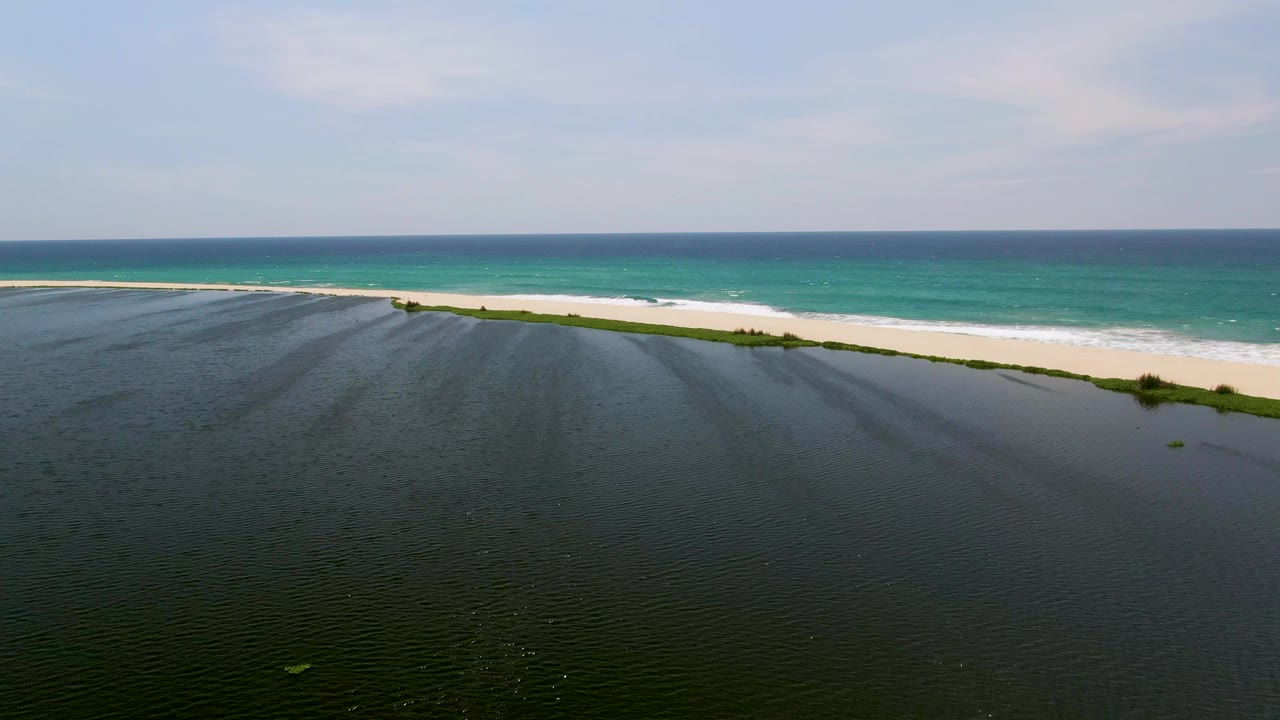Aerial beach scene with shallow lagoon-like water in front and ocean behind.