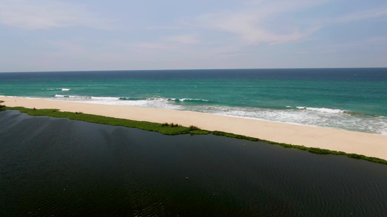 Aerial view of sandy beach between dark lagoon and turquoise ocean