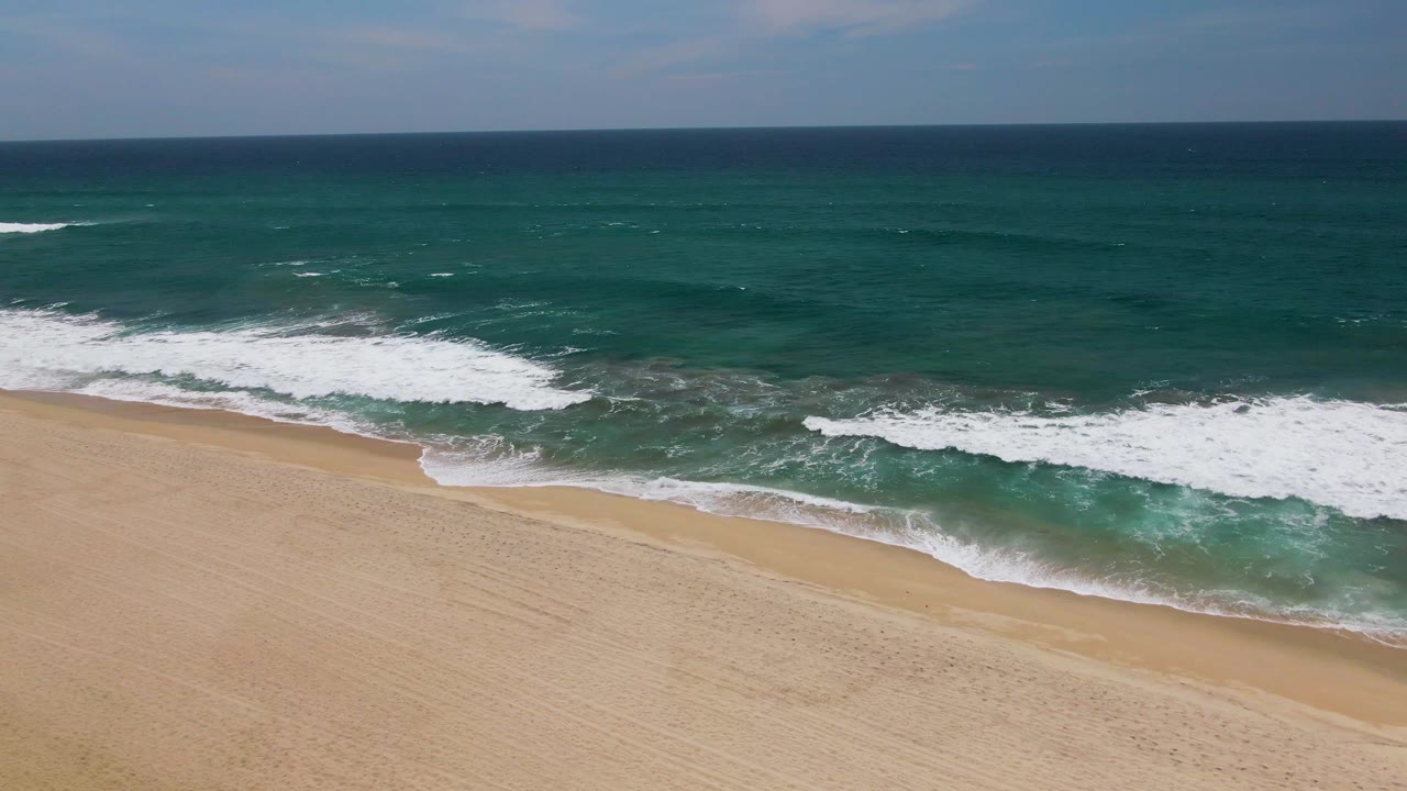 An empty sandy shoreline in San Jose Del Cabo sits below rolling blue-green waves, with a clean horizon and no visible people.