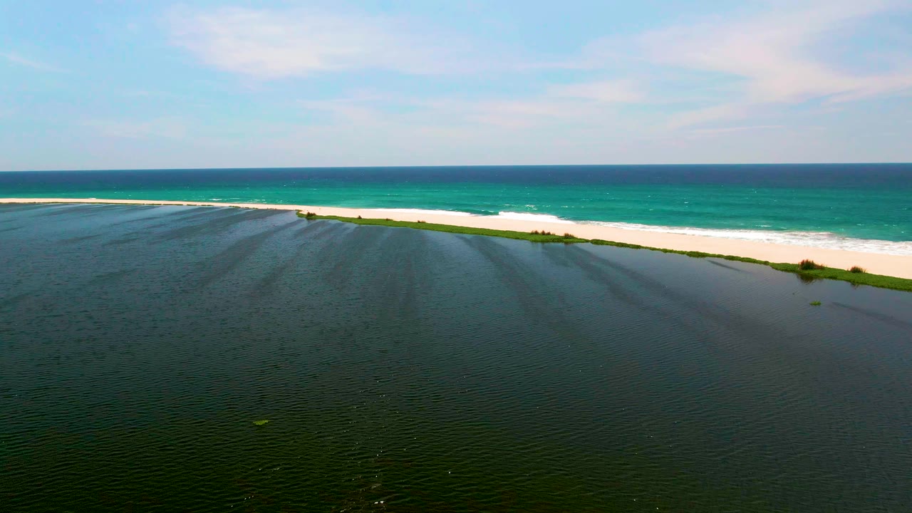 At two seconds, the San Jose del Cabo shoreline remains framed with rippled dark lagoon water below, bright sand and foam through the middle, turquoise sea beyond, and no visible people.