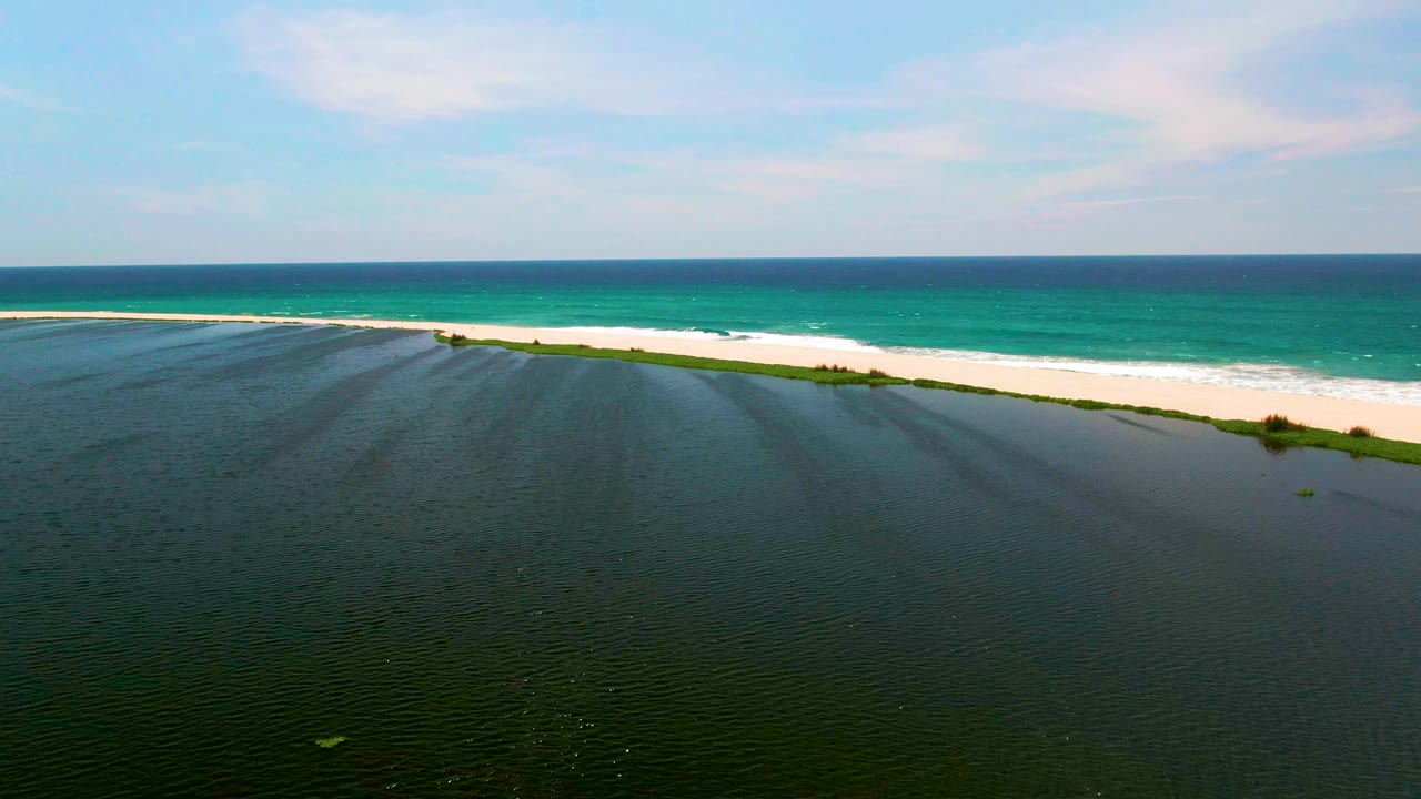 Aerial coastal view with lagoon ripples and foamy waves on a sand beach.
