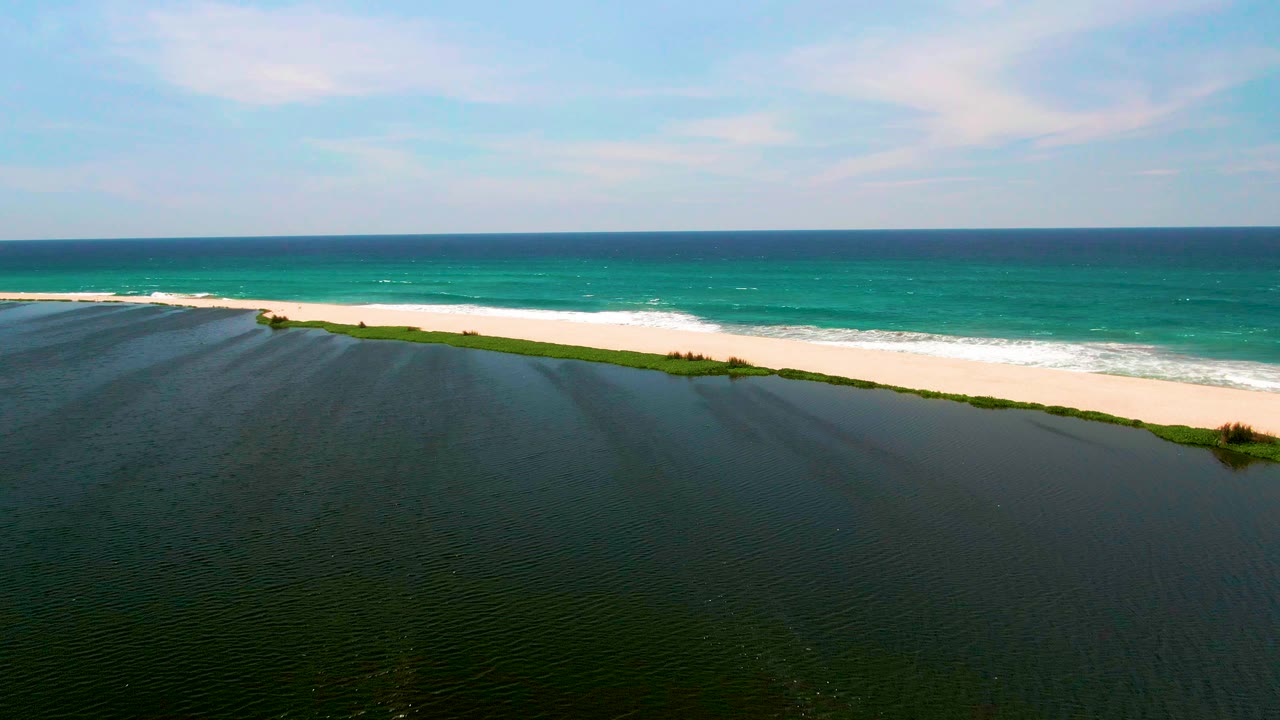 Lagoon and beach seen from above with ocean surf behind.