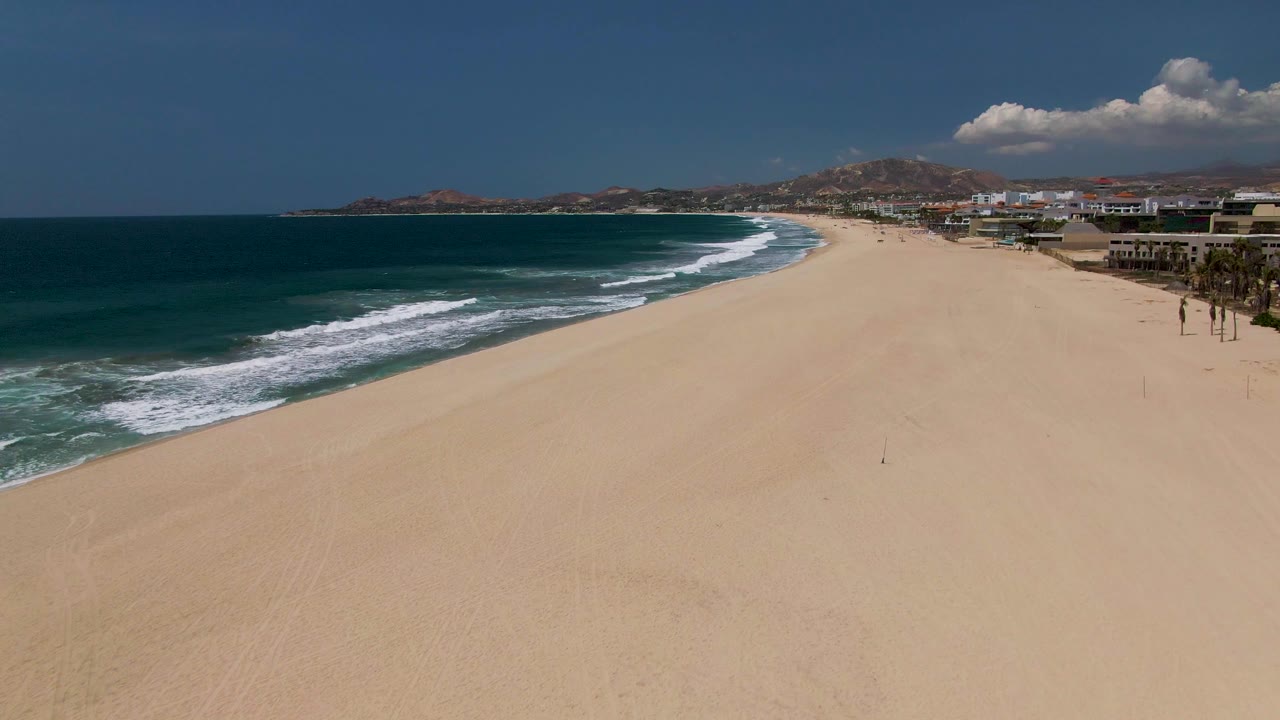 Aerial beach view with waves curving along a broad sandy shore.