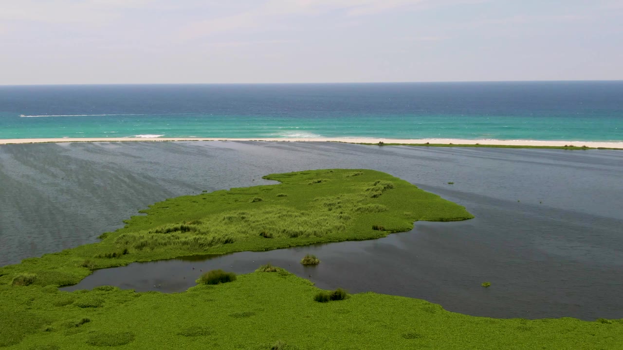 San Jose Del Cabo aerial frame with the island shifted slightly right in the lagoon and fine wave lines visible along the beach, no visible people.