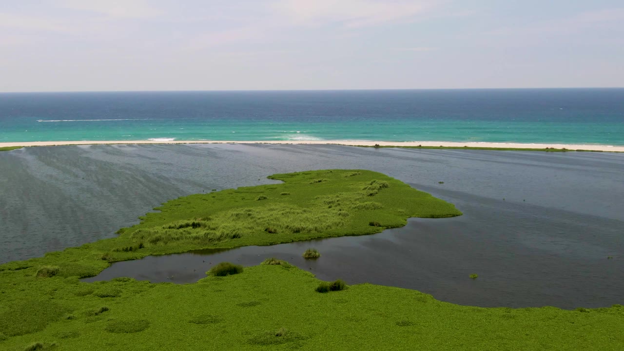 Green lagoon island below a white beach and blue ocean.