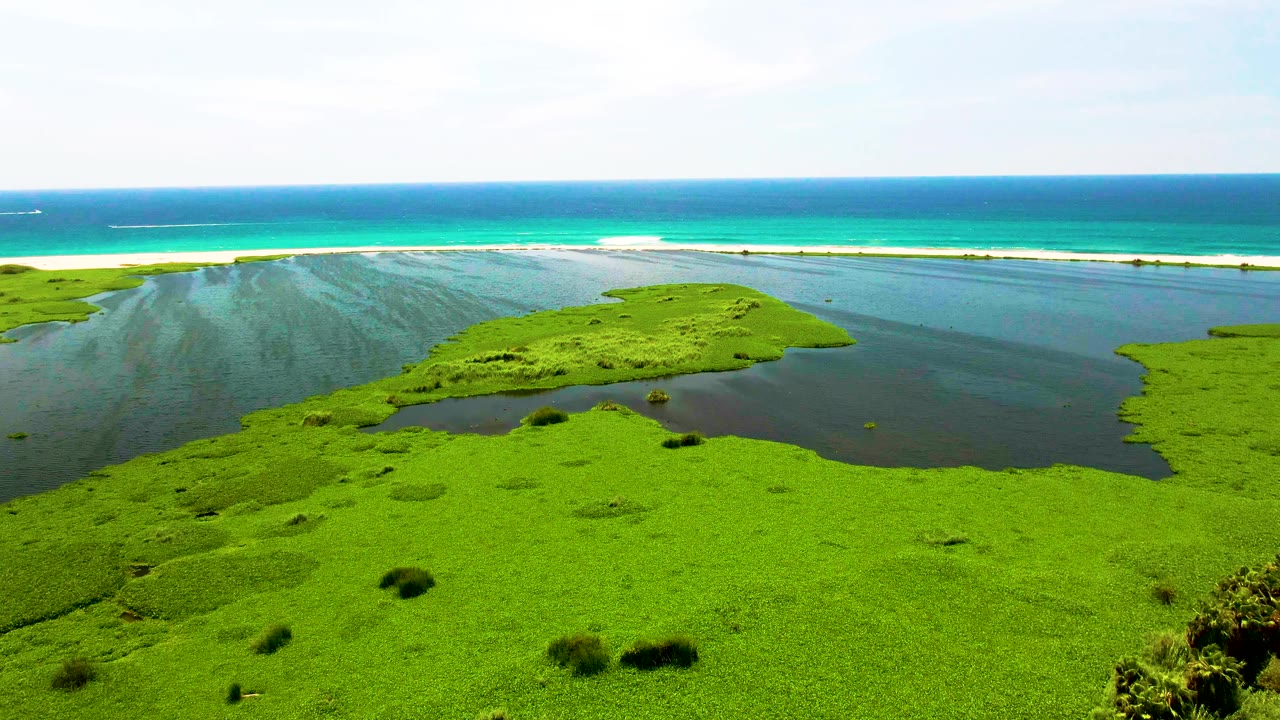 Wide aerial of lagoon water, green marsh, and distant ocean.
