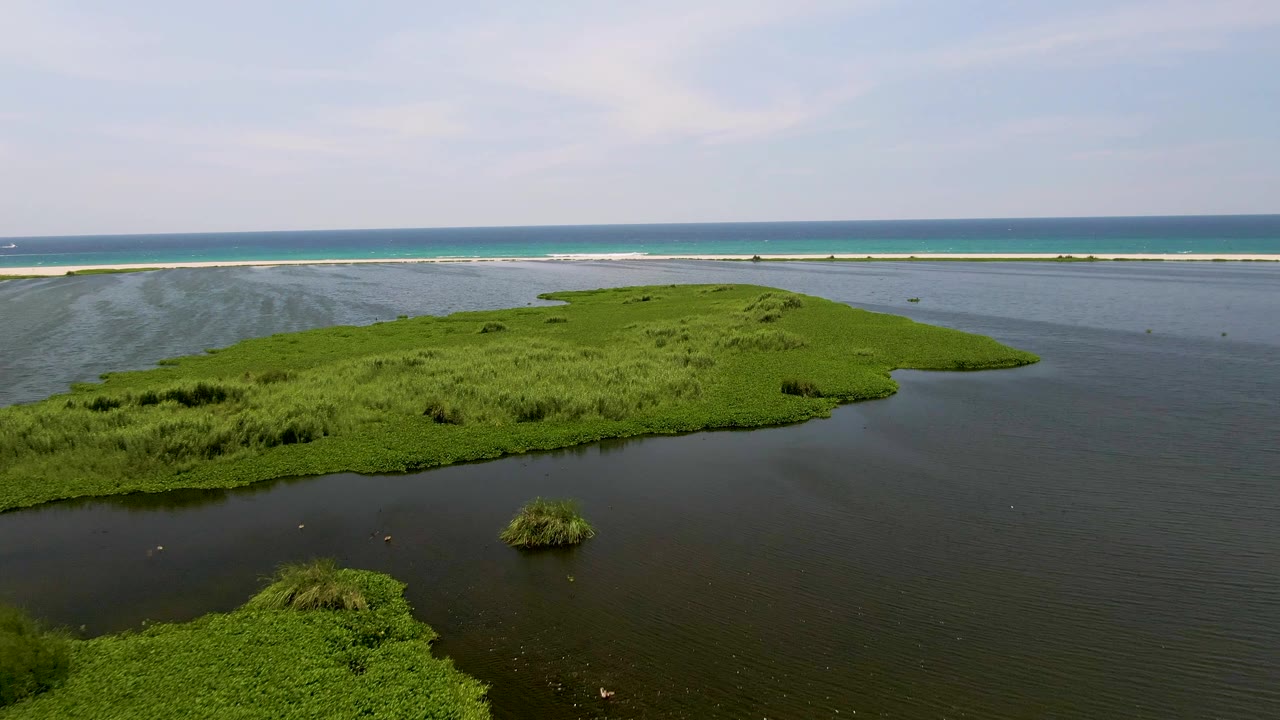 Aerial view in San Jose Del Cabo, Mexico, showing a lush green island in dark lagoon water with a pale sandbar, turquoise surf, blue ocean, and no visible people.