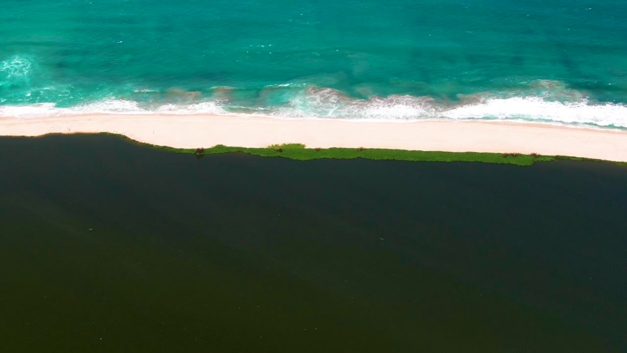 White wave foam spreads along a sandy shoreline under turquoise water.