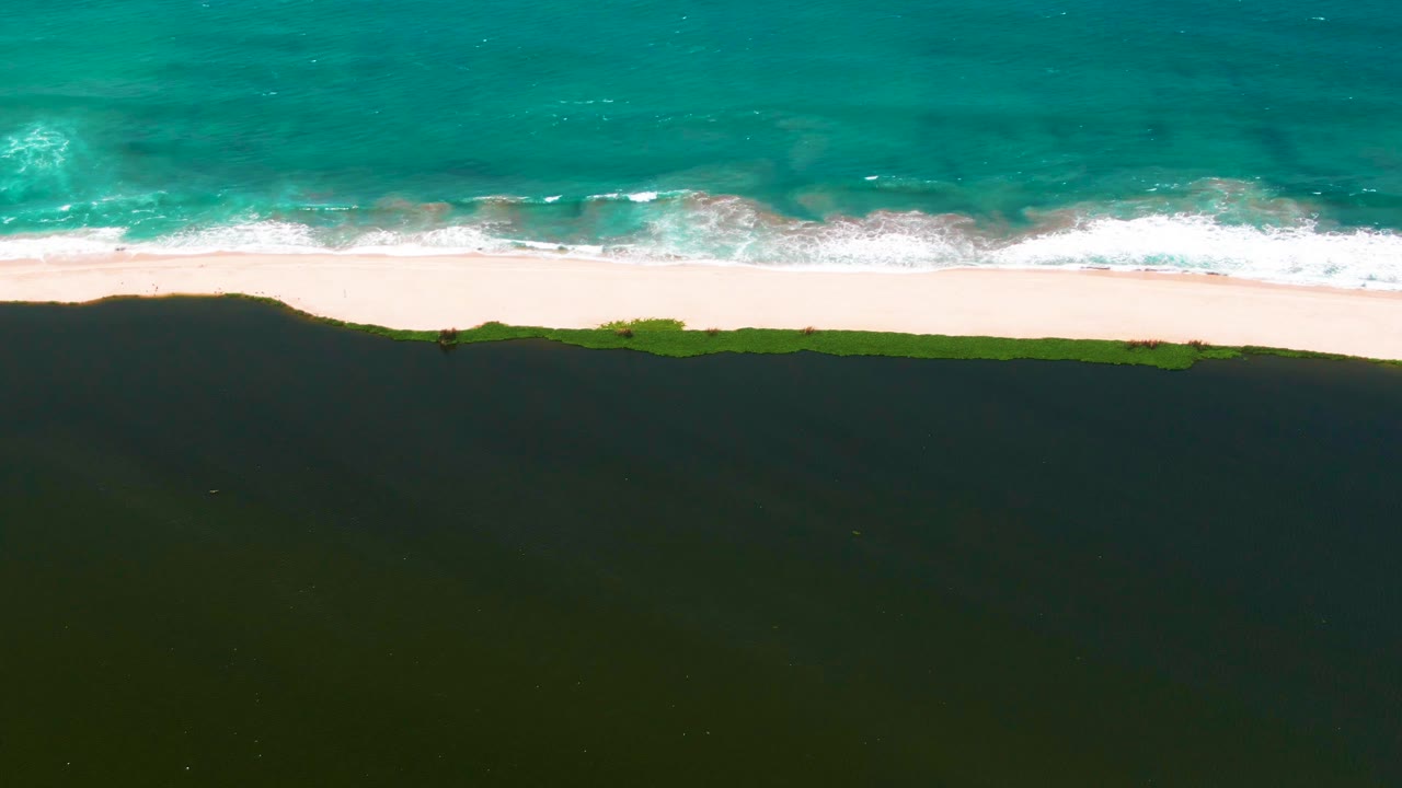 At 0:02, the San Jose del Cabo coast appears as horizontal bands of blue-green water, white surf, pale sand, a thin green strip, and darker land with no visible people.