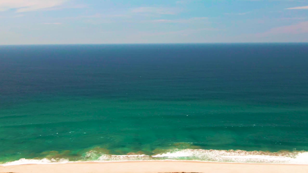 Ocean surf approaching a sandy beach below the horizon