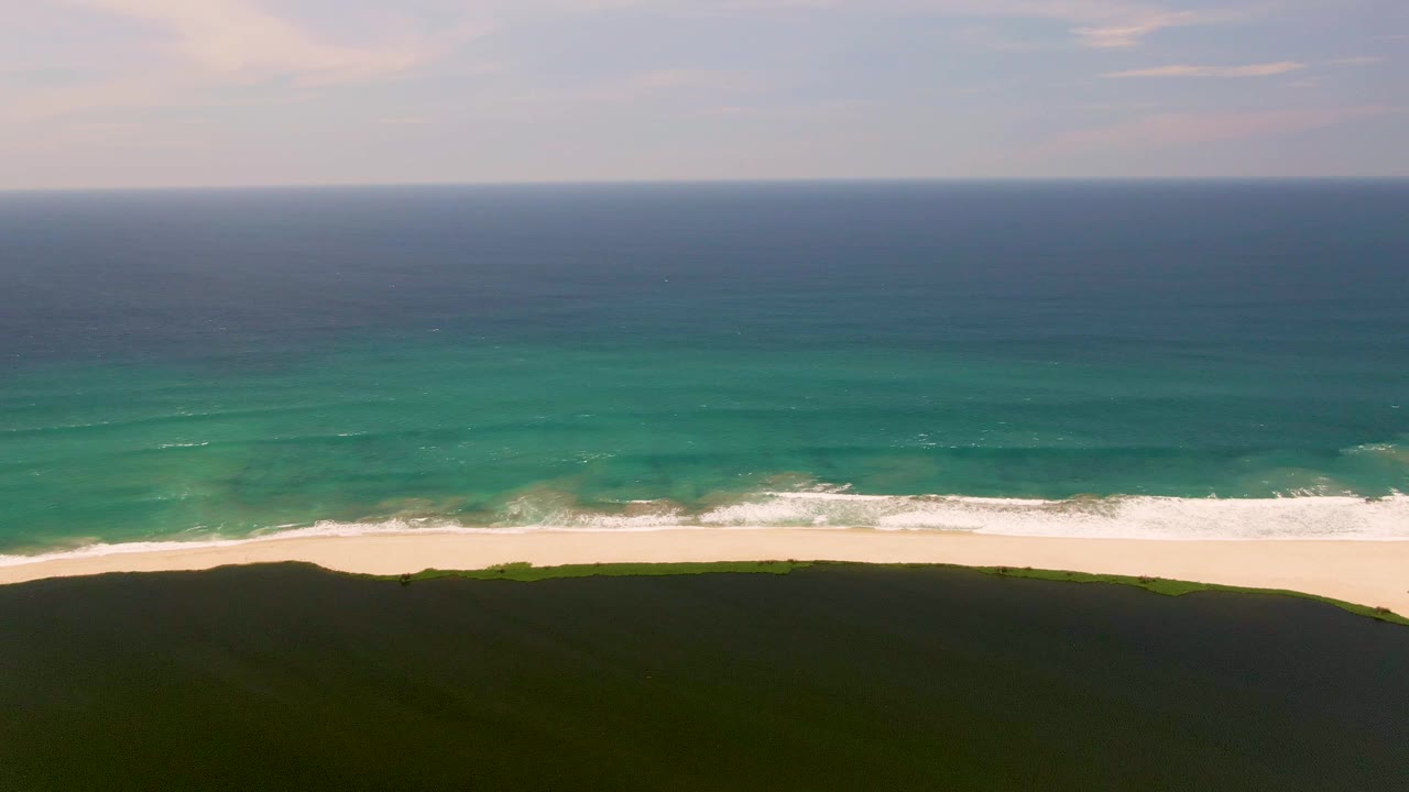 At three seconds, the San Jose del Cabo surf appears as uneven white foam along the sand, with green dune in the foreground, teal water beyond, and no visible people.